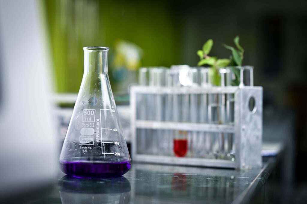 Close-up of a lab flask with purple liquid and test tubes in a scientific setting.